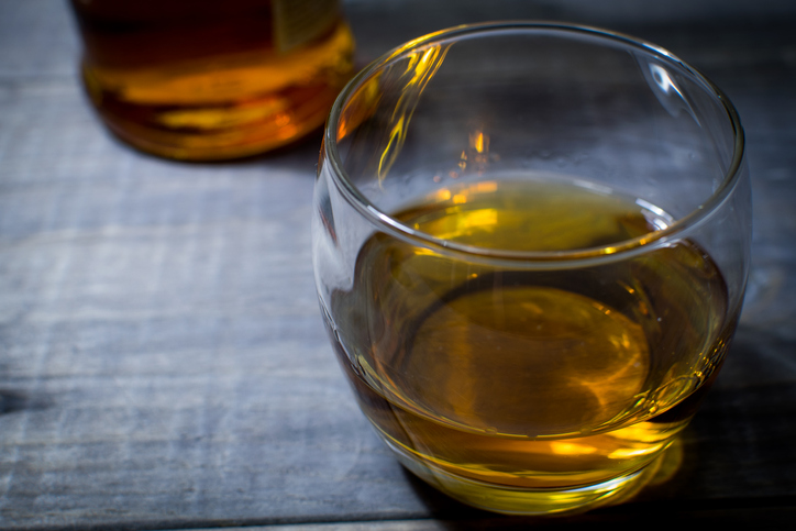 Glass of bourbon whiskey on the rocks against a vintage wooden table